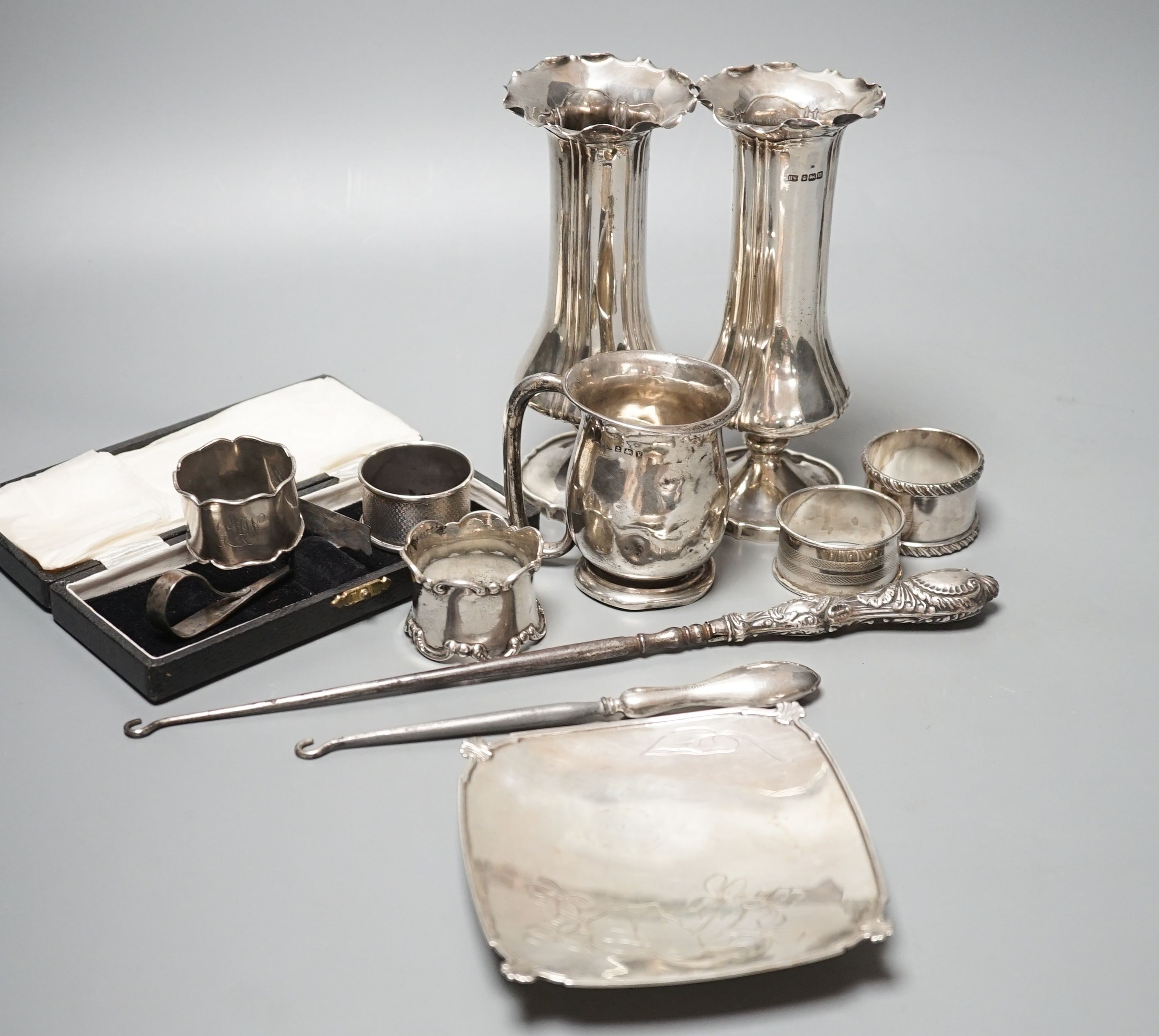 A pair of silver posy vases, a silver mug, a silver dish, five silver napkin rings, two button hooks and a cased silver pusher, weighable silver 9.5oz.